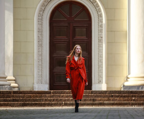 Elegant girl model in fashionable coat terracotta color goes on city street