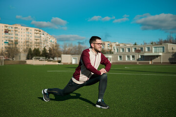 Young man in glasses stretching on a stadium. Exercising outdoors.