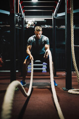 Fit man working out with battle ropes at fitness gym