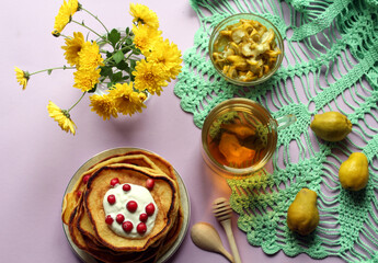 Quick Breakfast: fresh pancakes with cranberries, a Cup of tea, quince fruit - on an openwork napkin with a bouquet of chrysanthemums, top view