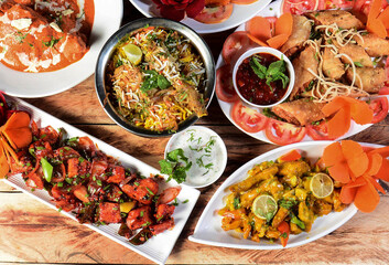 Assorted indian food on wooden background.Mutton biryani,lemon chicken,chilli chicken and spring roll.. Dishes and appetizers of indian cuisine