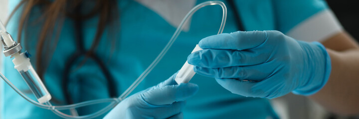 Close-up of female hands in sterile gloves putting dropper to sick patient. First aid procedures....