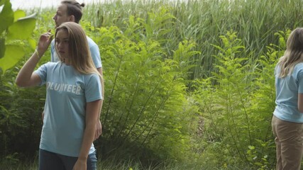Worried male and female volunteers searching something or someone in summer park or forest outdoors. Young Caucasian man and women walking in bushes and calling lost pet or kidnapped child.