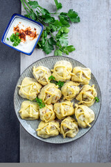 Traditional steamed Russian pelmeni with yoghurt cayenne pepper offered as top view on a rustic design plate