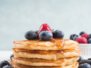 Stack of pancakes with fresh blueberries served in a dish with maple syrup being poured. Delicious breakfast.