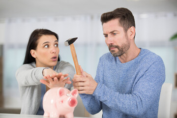 woman stopping husband from breaking piggy bank