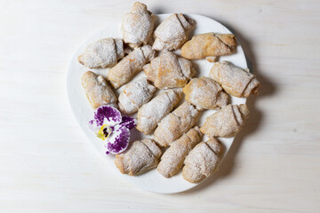 Heap of croissants and purple orchid flower on white plate