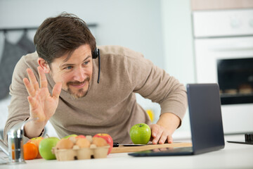 smiling happy man waving at laptop while cooking