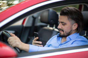 Handsome young man looking at the phone while driving