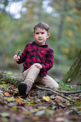 Little beautiful boy sitting on the ground in a forest hurt