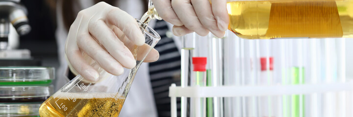 Close-up of laboratory worker pouring alcohol liquid in glass flask. Woman working in protective...