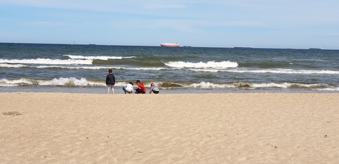 Czwórka dzieci nad brzegem morza odwrócona tyłem bawi sie w wodzie - obrazy, fototapety, plakaty