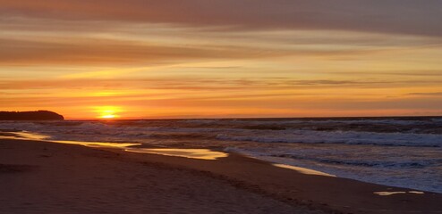 piekny zachód zlońca. Pomarańczowe niebo i cieple światło ślońca na piaszczystej plazy
