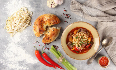 The Eastern cuisine. Uzbek soup. Lagman with lamb, noodles, vegetables,sauce, tandoor bread. Chili pepper, garlic, flour, spoon on gray background. Background image, copy space. Flatlay, top view