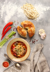 The Eastern cuisine. Uzbek soup. Lagman with lamb, noodles, vegetables,sauce, tandoor bread. Chili pepper, garlic, flour, spoon on gray background. Background image, copy space. Flatlay, top view