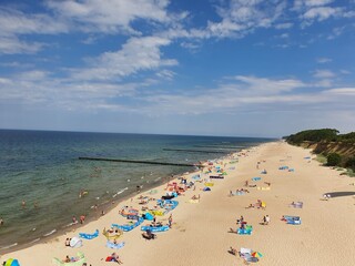 Widok na morze i plażę gdzie widać turystów. Kolorowe koce oraz parawany.