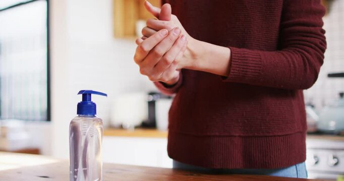 Mid section of woman sanitizing her hands at home