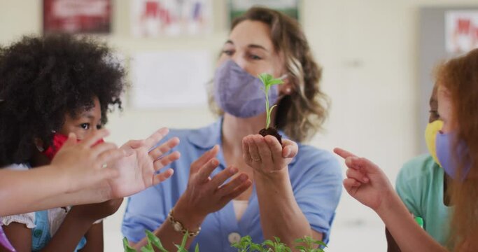 Female teacher wearing face mask showing plant sapling to students in class