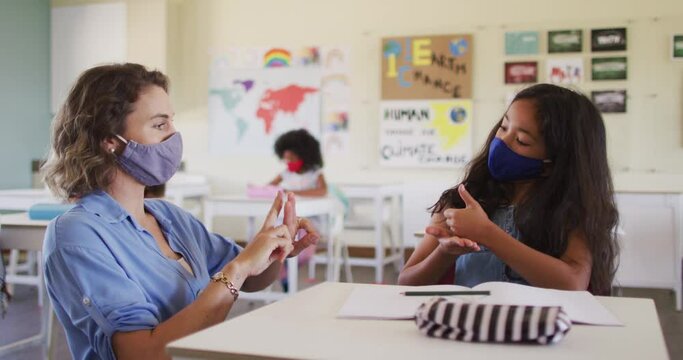 Female teacher and girl wearing face masks talking to each other through sign language in class