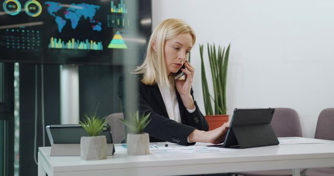 Close up of attractive confident high-skilled successful businesswoman which talking on phone and at a time working on i-pad