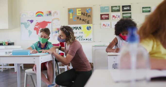 Female teacher wearing face mask teaching a boy in class at school