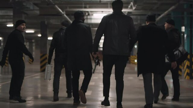 Back-view full footage of brutal assertive bandits walking down underground parking arguing and gesturing nervously looking around
