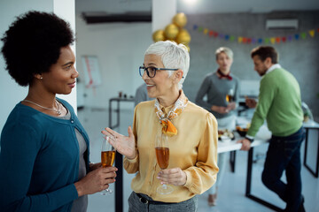 Two businesswomen talking while drinking Champagne at office party.