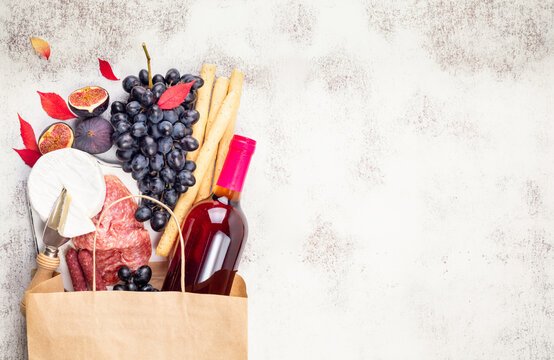 Rose wine and appetizers grape, figs, cheese camembert, bread stick, meat snaks on light background. Antipasto, gourmet, romantic, shopping food supermarket concept. Top view, copy space