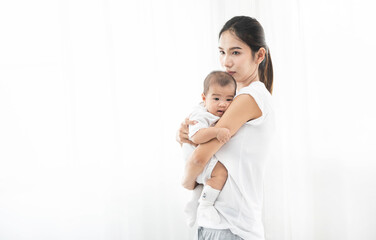 Pretty asian woman holding a newborn baby in her arms. Happy family. Laughing mother lifting her adorable infant baby son on white. 
