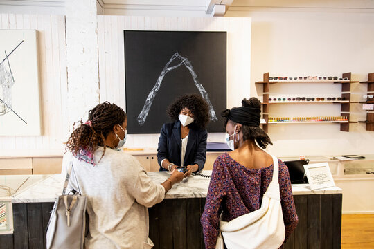 Female Shop Owner In Face Mask Helping Customers At Boutique Counter