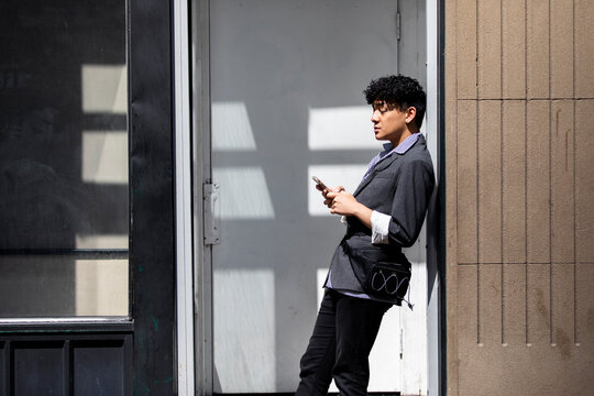 Stylish young man using smart phone in sunny doorway