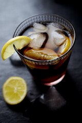 Glass of cola with lemon and ice cubes. Dark stone background. Close up.	