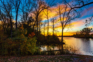 Beautiful golden hour sunset over a lake with a reflection and showing some fall colors and the silhouette of trees and leaves.