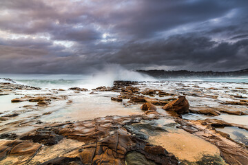 Rock platform, cascades and splashes with rain clouds by the seaside