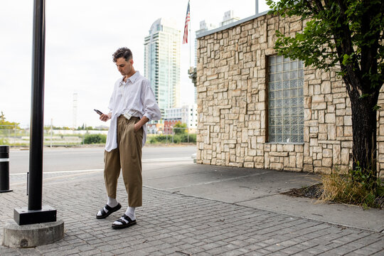 Stylish young man using smart phone on city sidewalk