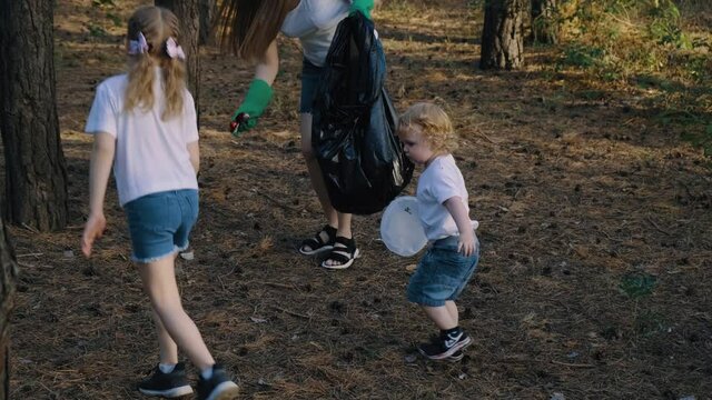 Mother with kids collecting trash in black bag in the park. Family collect plastic garbage. Picking up litter in the forest.