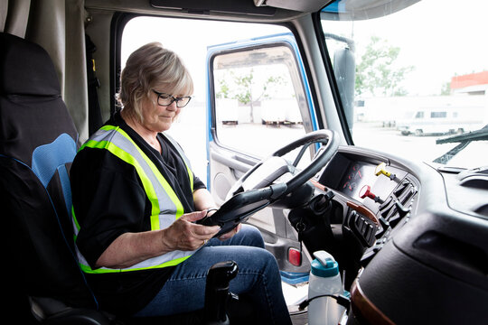Female trucker using digital tablet at wheel of semi truck