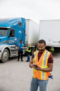 Warehouse worker texting on phone near container truck
