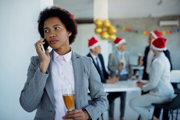 Pensive African American businesswoman talking on the phone at New Year's party in the office.