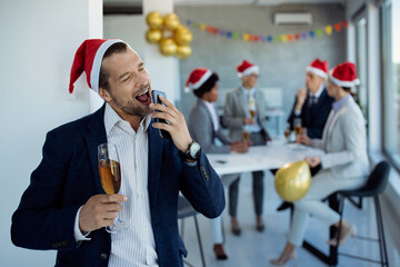 Playful businessman signing while using smart phone at Christmas party in the office.