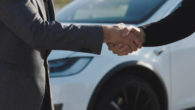 Dealer giving key to new owner in auto show or salon. Male hand gives a car keys to male hand in the car dealership close up. Unrecognized auto seller and a man who bought a vehicle shake hands.