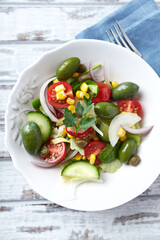 Healthy Salad with Green Olives, Baby Spinach, Cucumber, Cherry Tomatoes and Capers. Bright wooden background. Top view. Close up.	