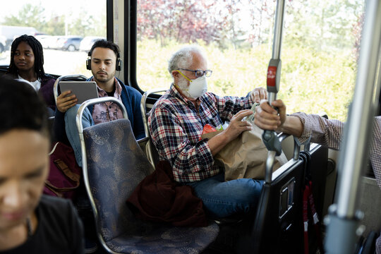 Senior male passenger in face mask using smart phone on public bus