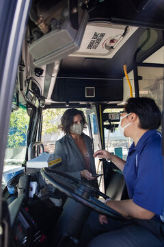 Bus driver in face mask greeting boarding passenger with smart phone