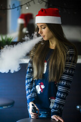 Vape teenager. Young pretty white caucasian girl in a hat of Santa Claus smoking an electronic cigarette in vape bar. Bad habit that is harmful to health. Vaping activity.