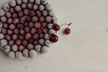 Frozen and fresh cherries on a light surface.