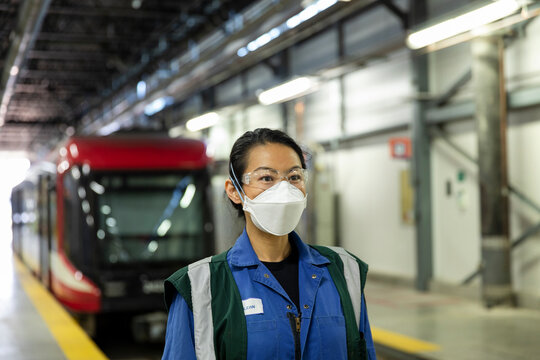 Woman wearing face mask standing on railway platform in subway train workshop