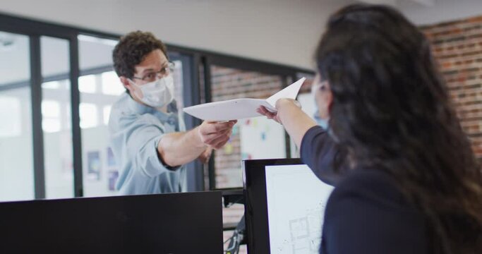 Man wearing face mask passing a document to his colleague at office