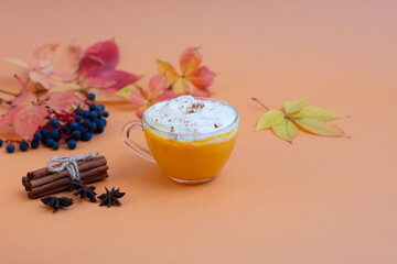Pumpkin spice latte in a glass mug with whipped cream on  beige background. Autumn leaves. Hot autumn drink.