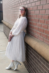 Beautiful, Young 30 Years Old Girl with Blonde Hair, in Glasses, wearing white dress, Smiling and Posing for camera, red Bricks background, Happy Woman  